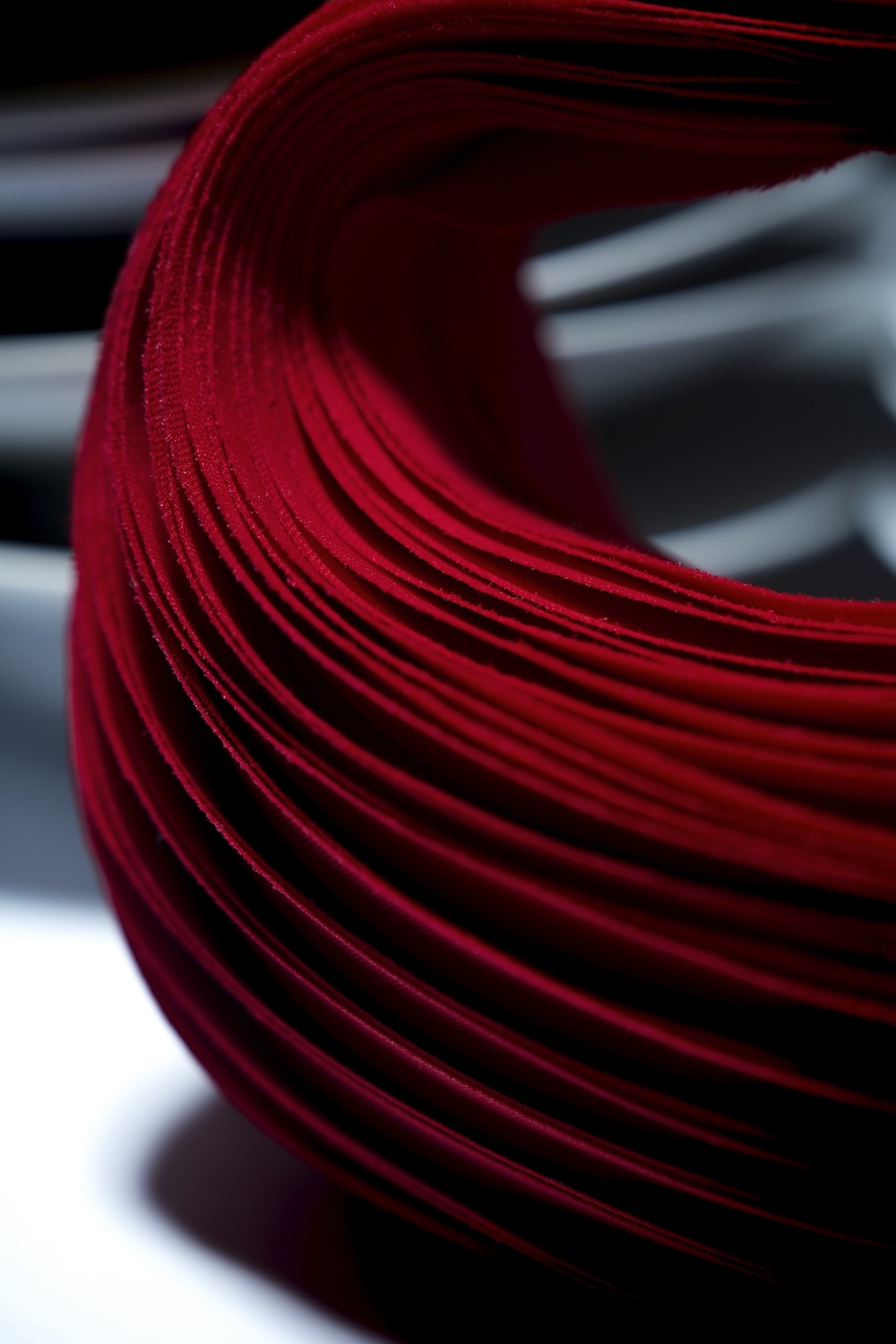 Close-up of a curved stack of red paper sheets, creating an abstract pattern with dramatic shadows and highlights.