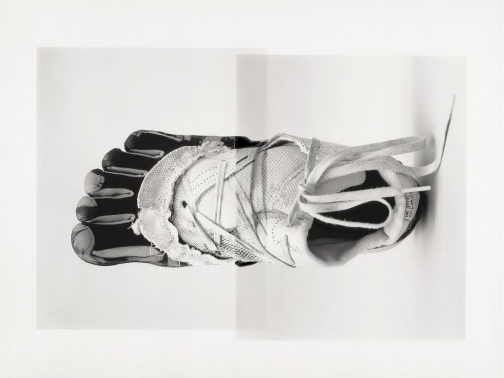 A black-and-white photo shows a foot wearing a minimalist, toe-separating athletic shoe that appears worn and torn, viewed from above against a plain white background.