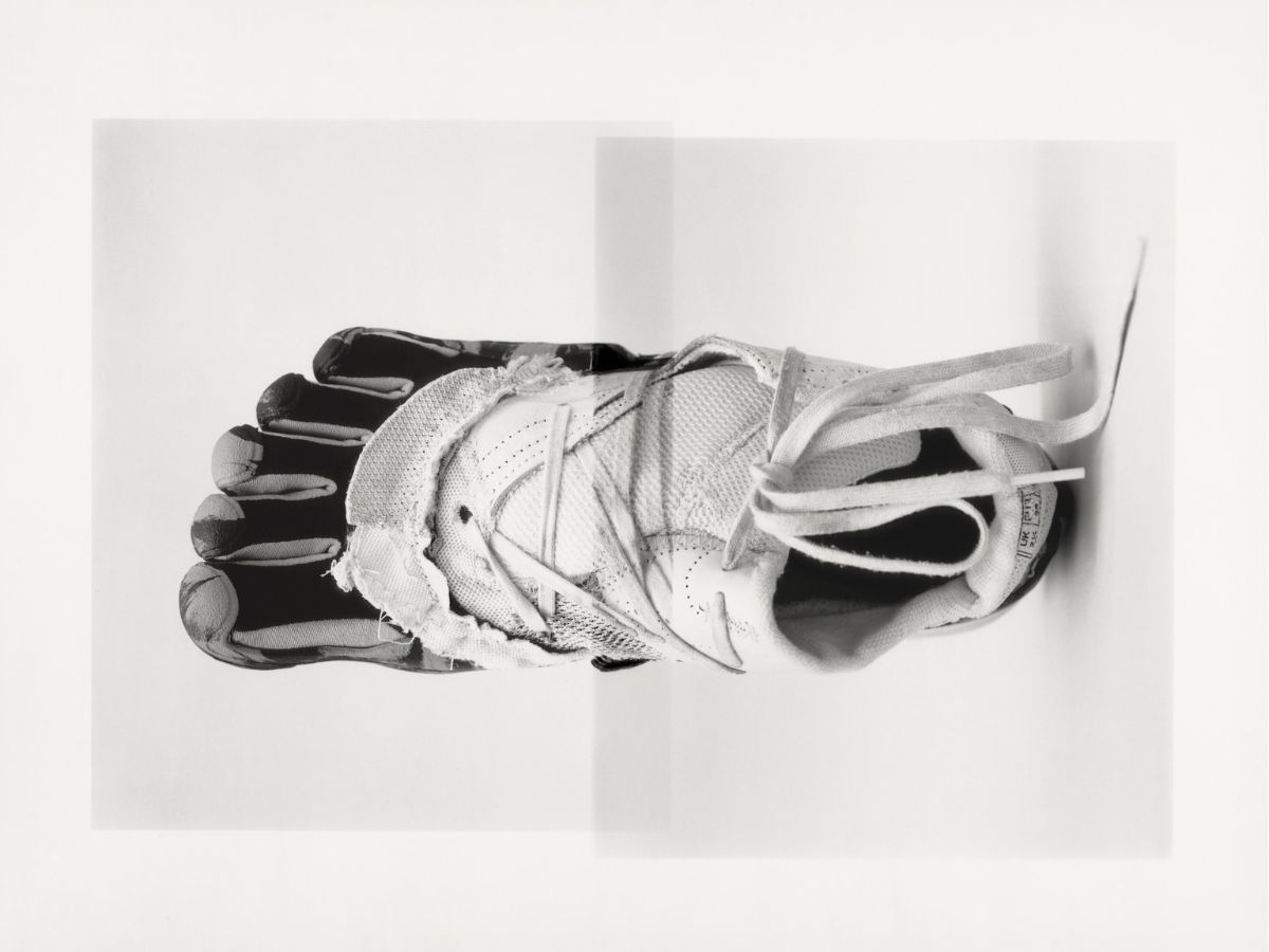 A black-and-white photo shows a foot wearing a minimalist, toe-separating athletic shoe that appears worn and torn, viewed from above against a plain white background.