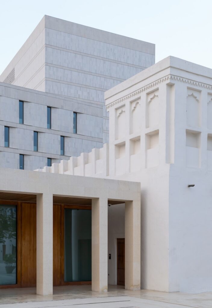 Modern and traditional white buildings with clean lines and minimalistic architectural details reminiscent of Msheireb; the façade includes wooden doors and geometric window patterns.