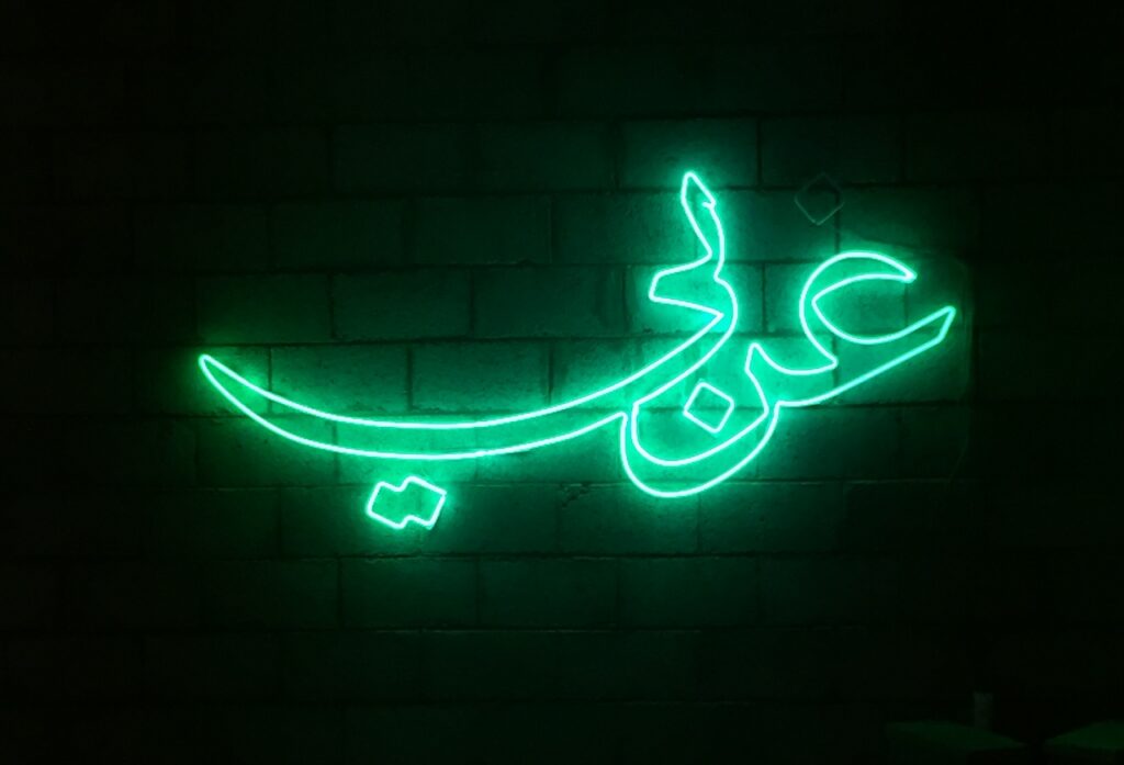 Neon green Arabic script glows on a dark brick wall, channeling gulf futurism with its vibrant, forward-thinking energy.