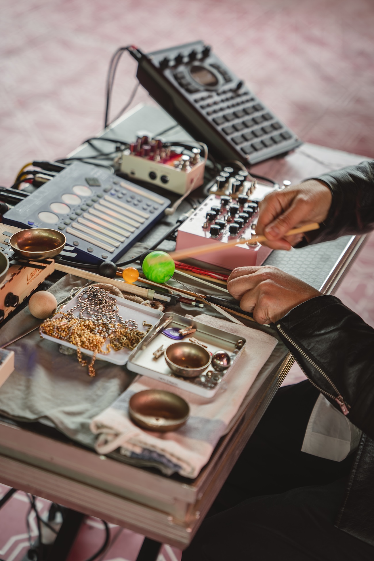 A person uses mallets to play various small percussion instruments and electronic equipment on a table, including singing bowls, chimes, sound mixers—and even a Fashion Trust Arabia Prize-inspired bell for a creative twist.