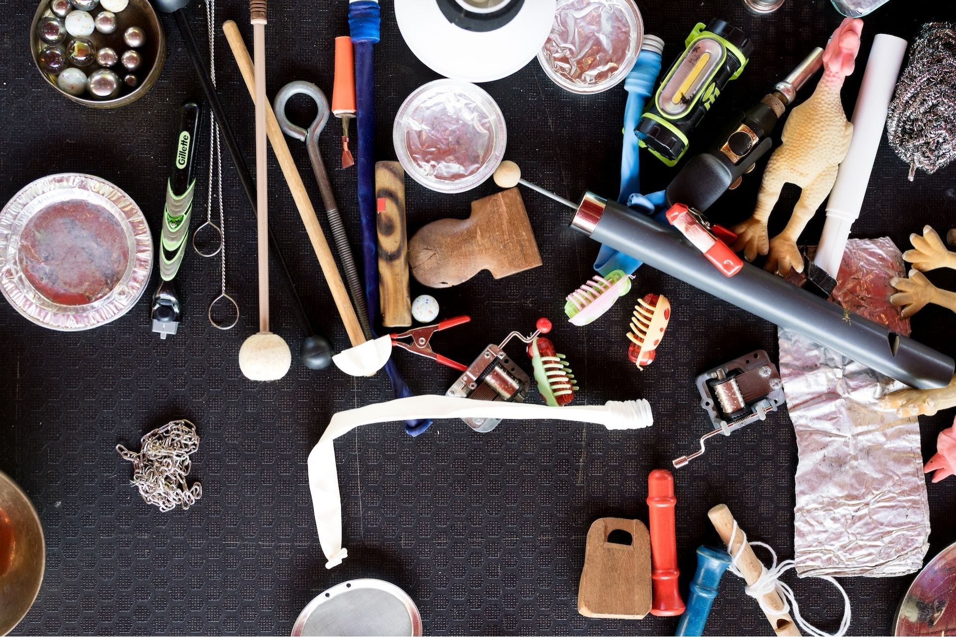 A variety of assorted objects on a black surface, including toy skeletons, musical mallets, rubber chickens, metal chains, tools, tin foil, goggles, and small containers—an arrangement as eclectic as the Fashion Trust Arabia Prize.
