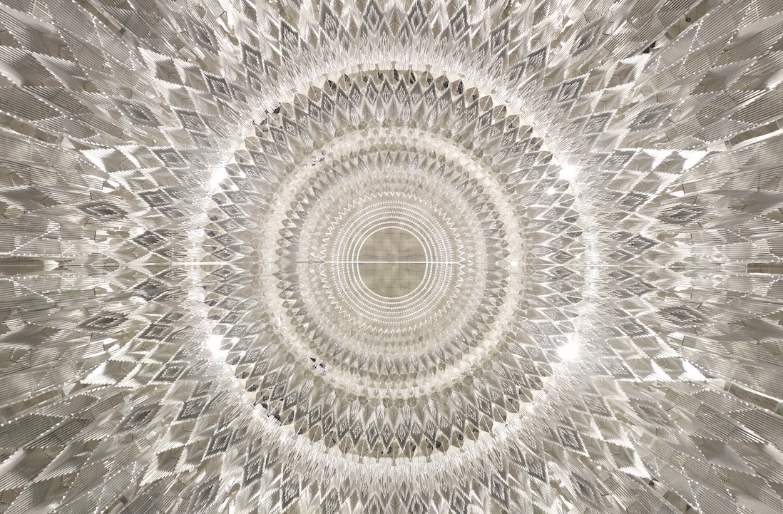 Symmetrical concentric diamond patterns radiate outward in a circular, kaleidoscopic design, creating a sparkling, glass-like or crystal chandelier effect with a bright central focal point.