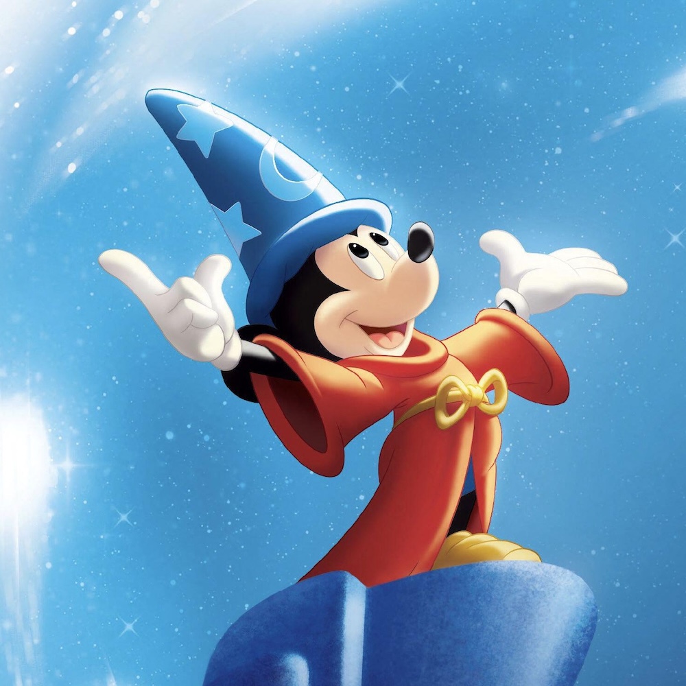 Animated mouse in a red robe and blue wizard hat stands on a rock with arms raised, smiling against a magical blue background