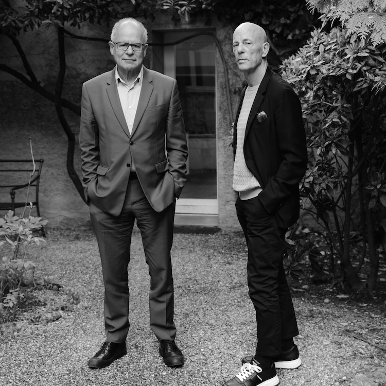 Rirkrit Tiravanija and another man in formal blazers standing in a garden setting.