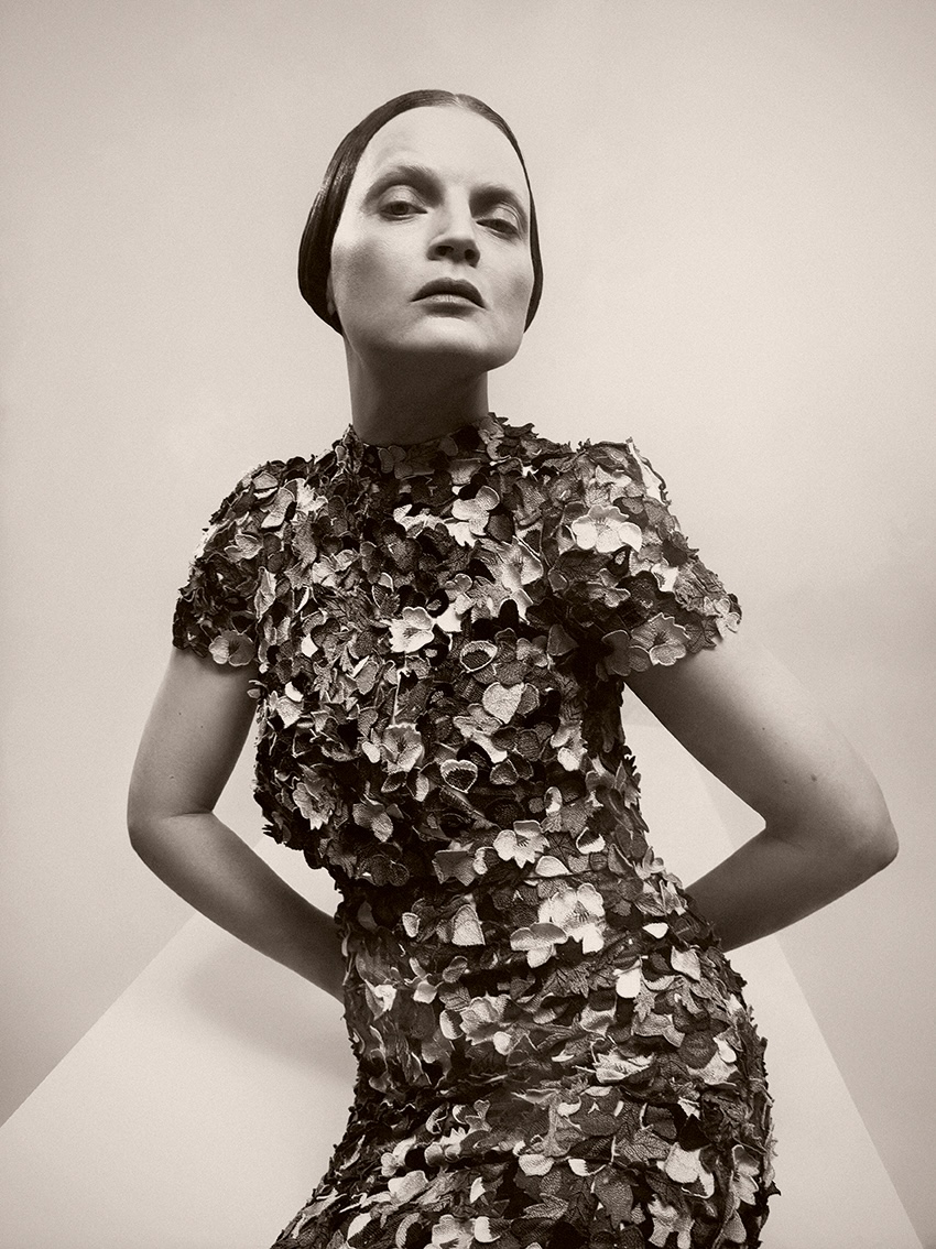 A person poses confidently in a short-sleeved dress covered in textured floral patterns. The portrait is in black and white, creating a dramatic and elegant mood.