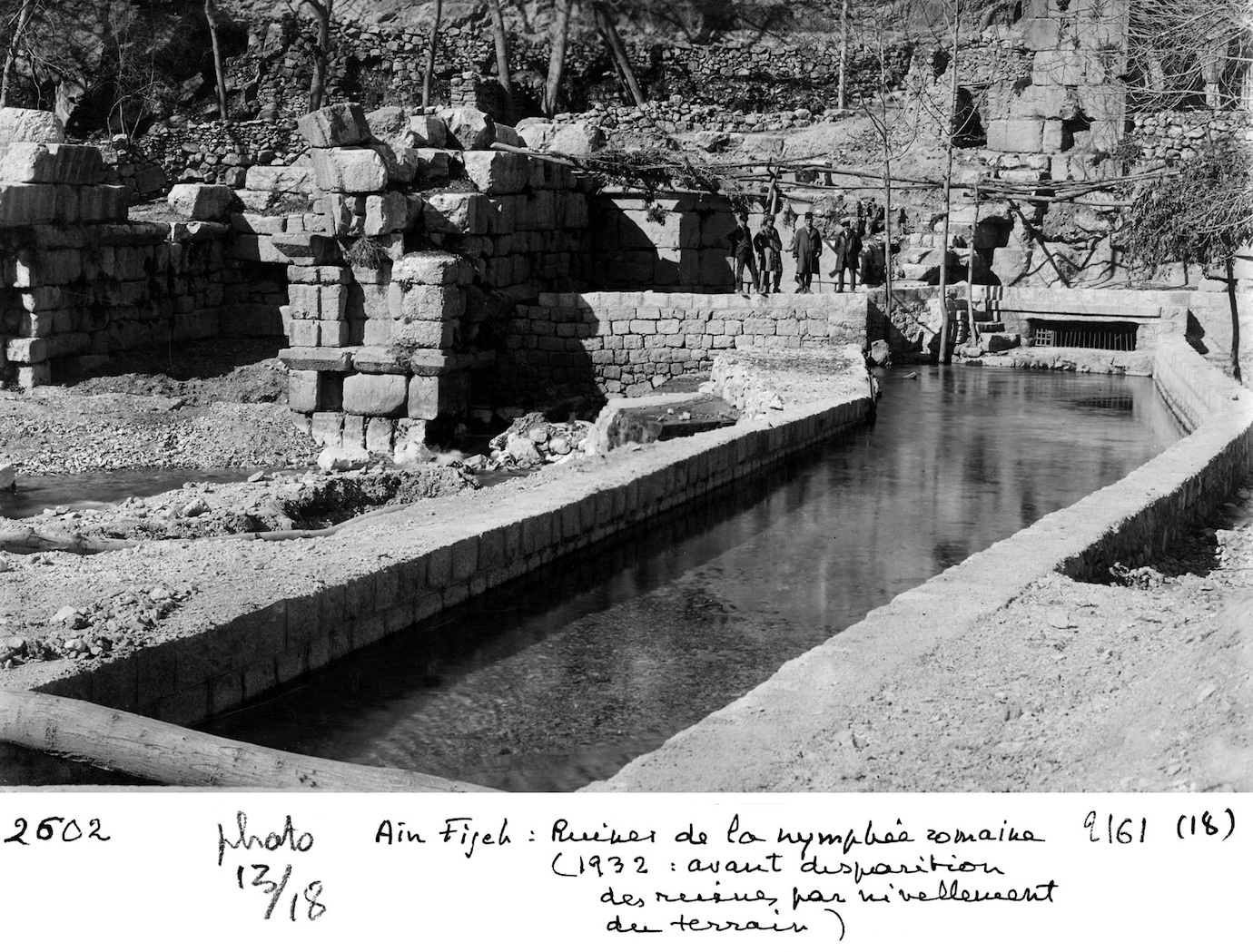 Black and white photo of ancient stone ruins beside a shallow water channel.