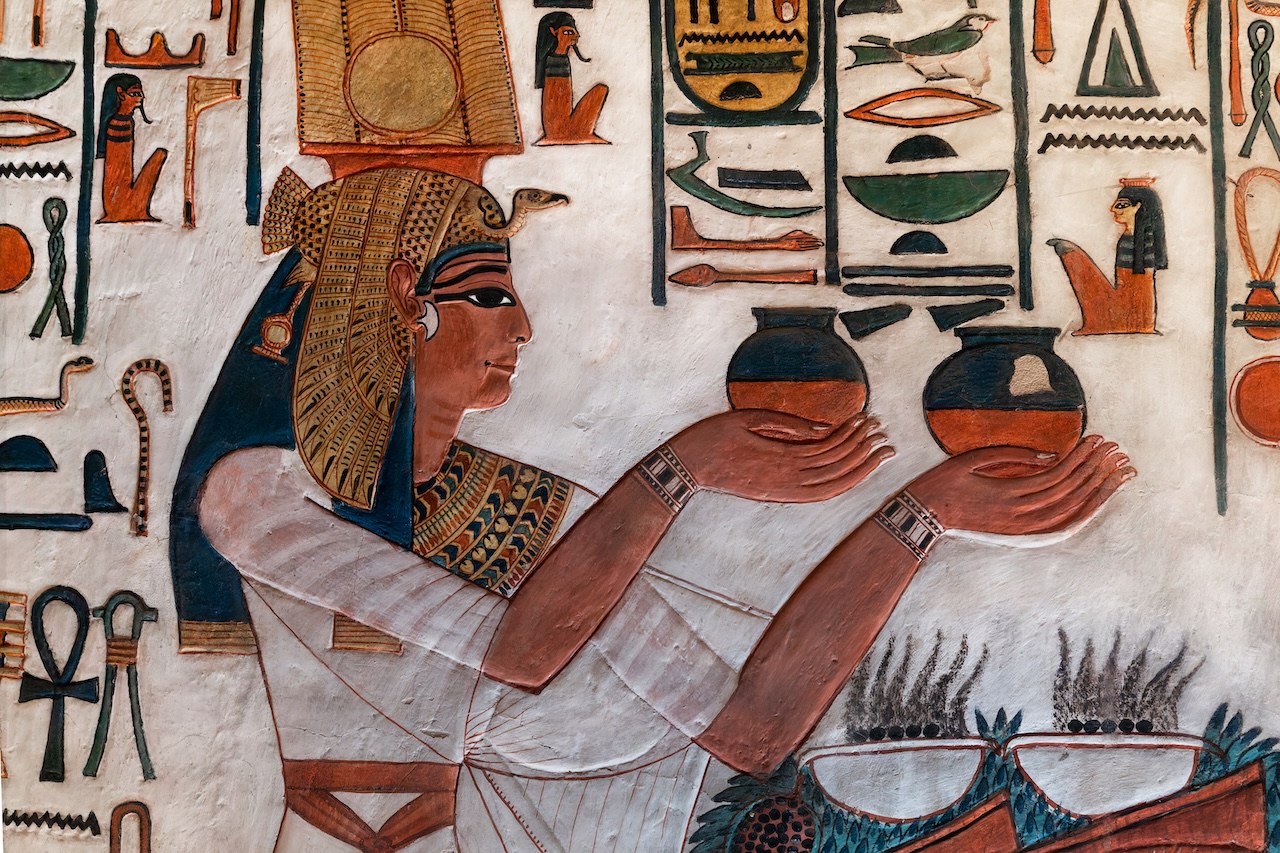 An ancient Egyptian wall painting in the style of Luis Monreal, depicting a queen in profile offering two rounded vessels, surrounded by hieroglyphic symbols.