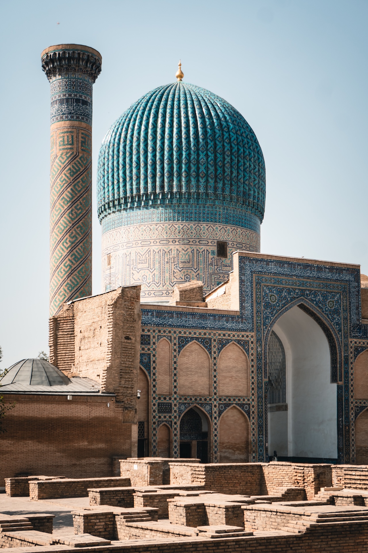 The Gur-e-Amir mausoleum, as documented by Luis Monreal, features a large ribbed blue dome and a tall, ornate minaret set against a clear sky.
