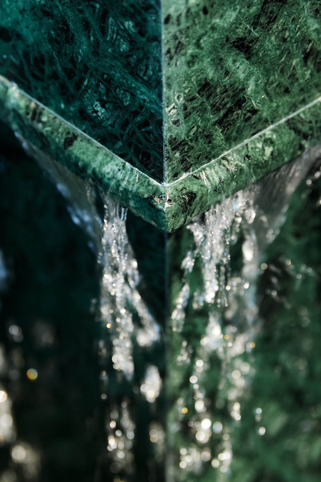 Close-up of water cascading down the corner of a textured green marble fountain, with light reflecting off the flowing water