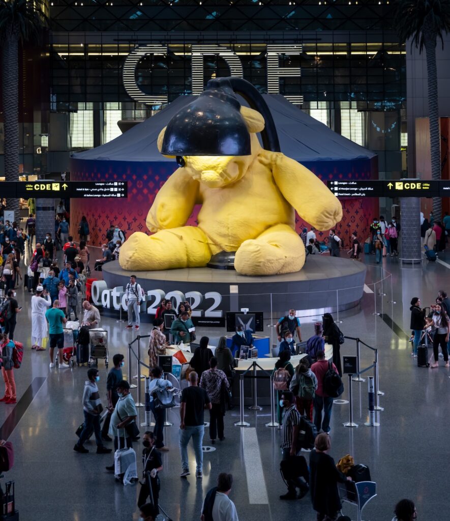 A large yellow teddy bear sculpture with its head under a black lamp