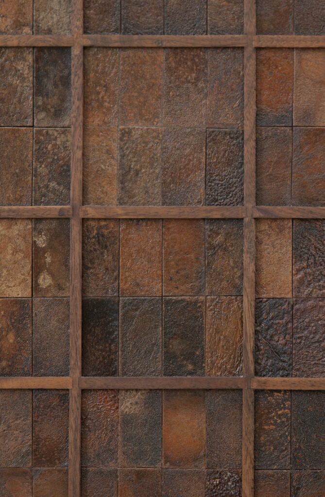 A grid of square, textured tiles in earthy brown and rust shades, separated by wooden dividers, creates a geometric, rustic pattern
