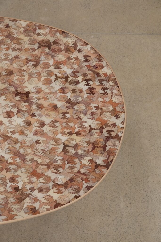A tabletop with an intricate inlay pattern of small, multicolored wooden leaves in shades of brown, beige and tan