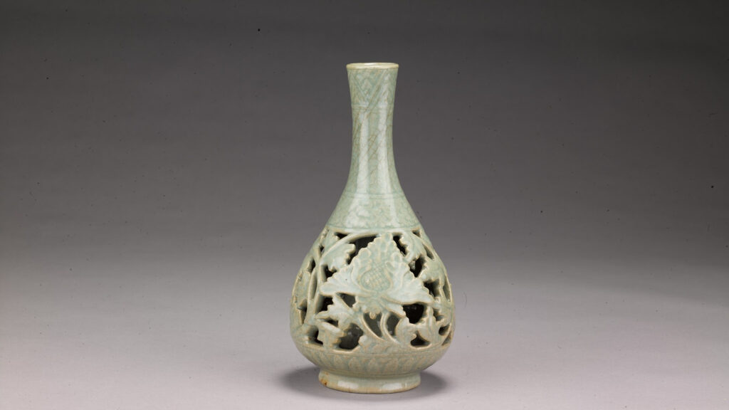 A pale green celadon ceramic vase, typical of those found in Qatar, with a long neck and a bulbous base featuring intricate openwork floral carvings.