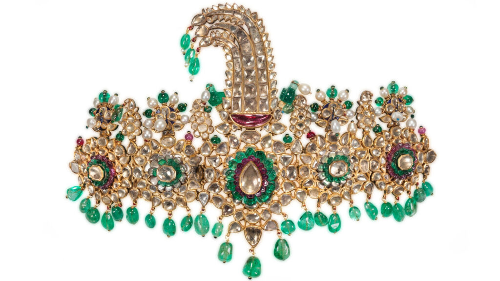 A traditional Indian gold necklace set with uncut diamonds, emeralds, pearls, and a central ruby, featuring a prominent, curved paisley-shaped pendant, reminiscent of classic jewelry styles found in Qatar.